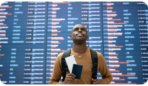 Photo of an expat holding his passport at the airport in front of the flights screen
